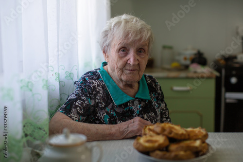 An elderly old woman drinking tea in her kitchen at home.