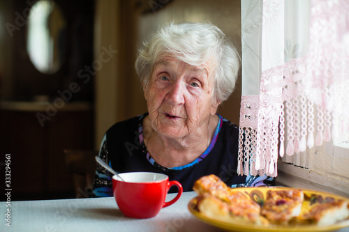 An elderly old woman has breakfast sitting at her home.