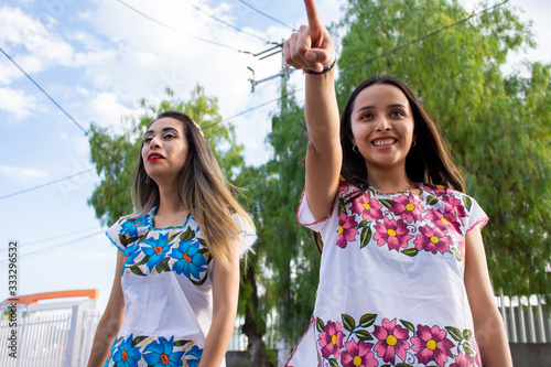 Two young women wearing traditional mexican clothes walking and having fun on the street