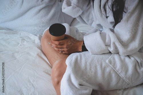 Young girl in white bathrobe is holding a cup of coffee. Morning time. Bride. Manicure. Ring on a her finger. Weekend time.