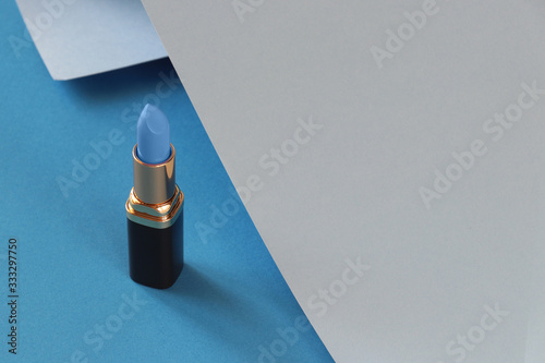 Blue lipstick, grey, blue background. Beautiful blue lipstick on a blue background with grey rolled-up paper. Trendy concept. Blue and grey. photo