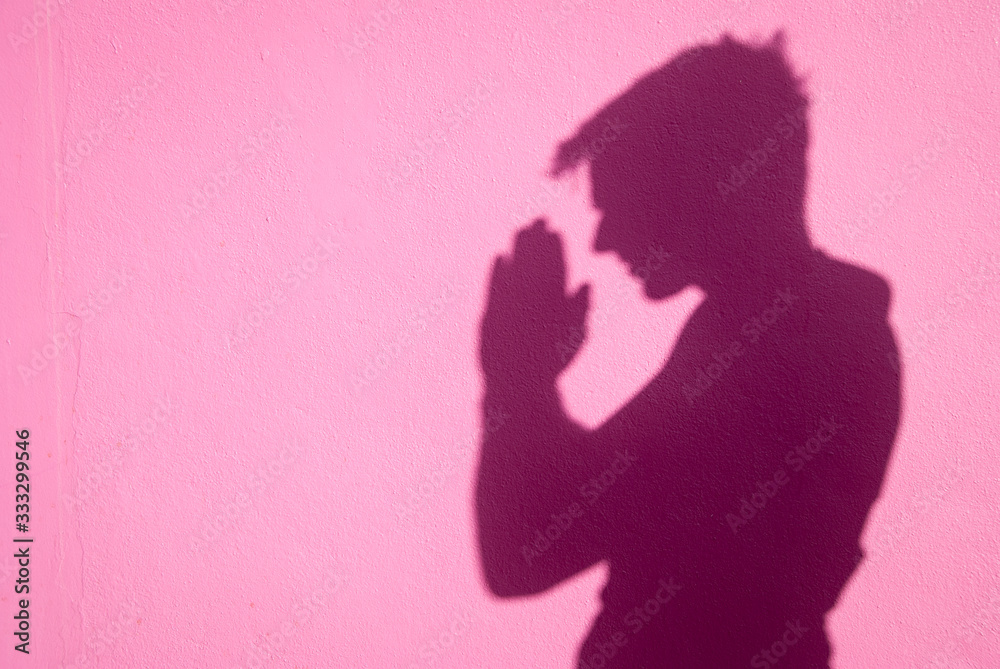 Portrait of unrecognizable shadow man holding his palms together in gratitude on a bright pink wall