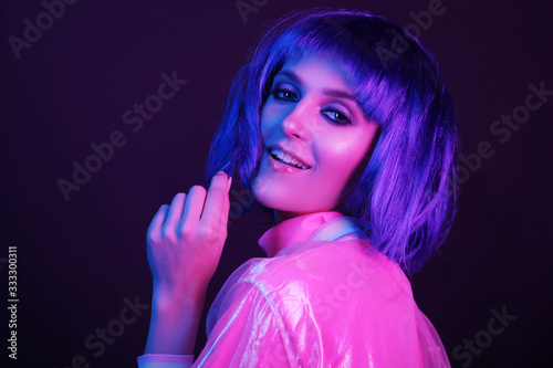 Neon light studio close-up portrait of happy woman model in a wig. Nightlife, party in a nightclub. Copy space.