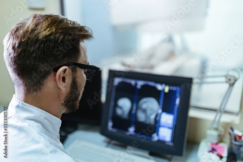 Doctor supervising brain MRI scan examination of a patient from control room.