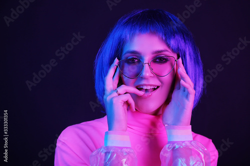 Neon light studio close-up portrait of happy woman model in a wig in sunglasses. Nightlife, party in a nightclub. Copy space.