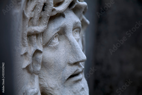 Ancient statue of Jesus Christ in profile against dark background. Religion, faith, death God concept.
