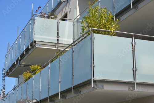 Balkon mit Edelstahl-Geländer und Sichtschutz aus Milchglasplatten an der Fassade eines modernen Mehrfamilien-Wohnhauses
