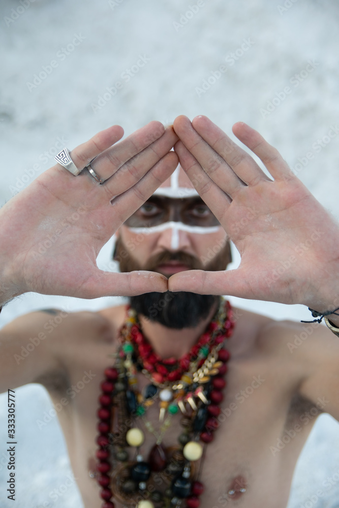 young man with primal makeup and beads spells with powder in hands on white rocks
