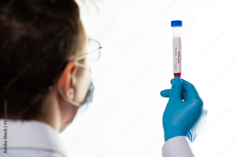 Fototapeta premium Test tube in male hand close up, doctor in medical mask holding vial with red liquid. Concept blood sample, coronavirus diagnostic, medical research