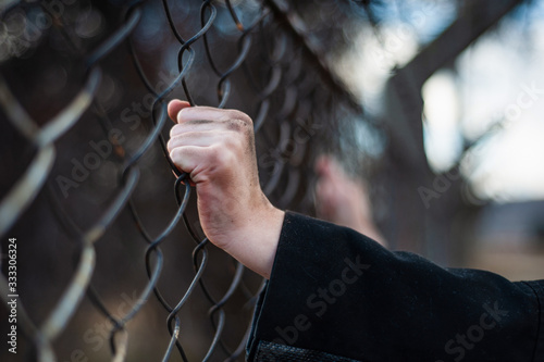 The migrant is holding his hands behind the protective fence