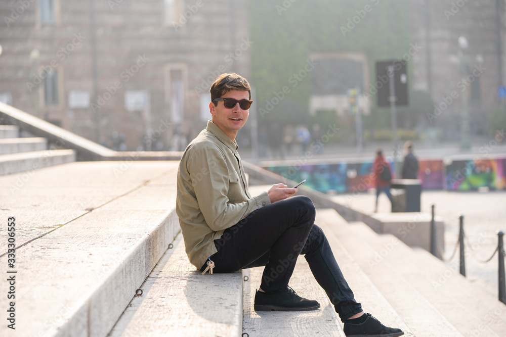 Portrait of young smiling man isolated on outside outdoor background uses a cellphone, sun glasses Portrait of young smiling man isolated on outside outdoor background uses a cellphone, sun glasses