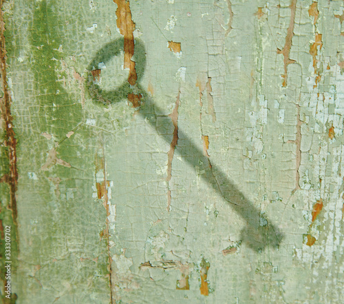 The shadow of the key on the old wooden surface. The wood texture is visible through the peeling green paint.