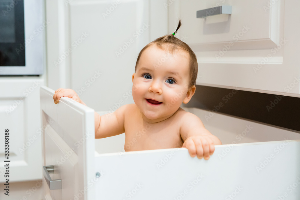 Happy baby girl smiling sitting in kitchen drawer with pans Happy baby girl smiling sitting in kitchen drawer with pans