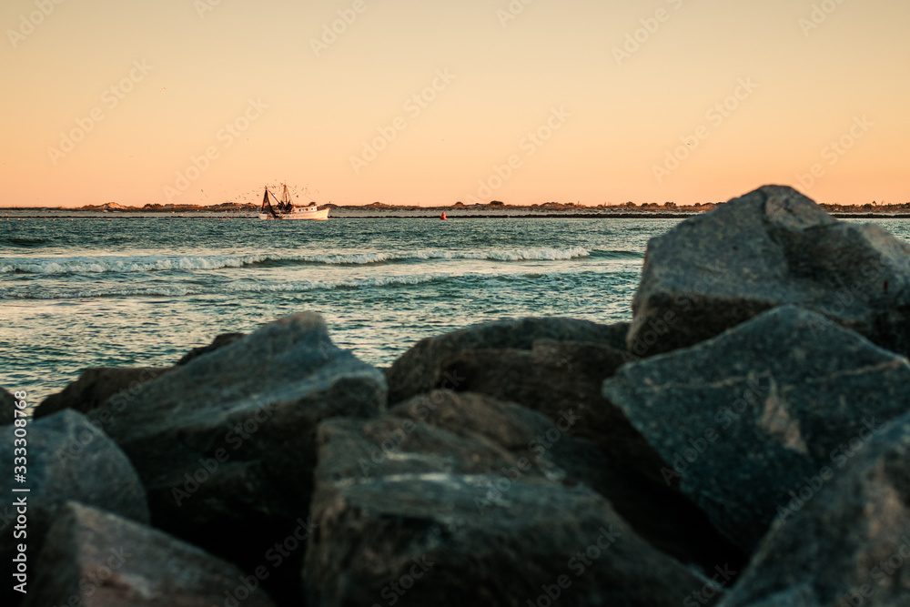 Shrimper Sailing Home in Golden Hour Light with Large Rocks in Foreground Shrimper Sailing Home in Golden Hour Light with Large Rocks in Foreground