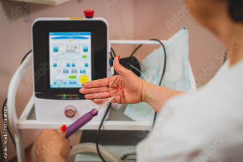 Female doctor is holding a laser used for vaginal treatment of incontinence, Visible ray of laser beam in a hand shaped as a vaginal entrance. Laser control screen seen in the background.
