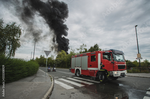 Photo of a fire next to a motorway in Stegne  Ljubljana  Slovenia. Dark plume of smoke is visble rising up from the place of ignition with red fire truck seen in the foreground.