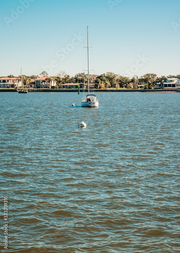 Small Sailboat Lying At Anchor with Houses Along the Coast Behind