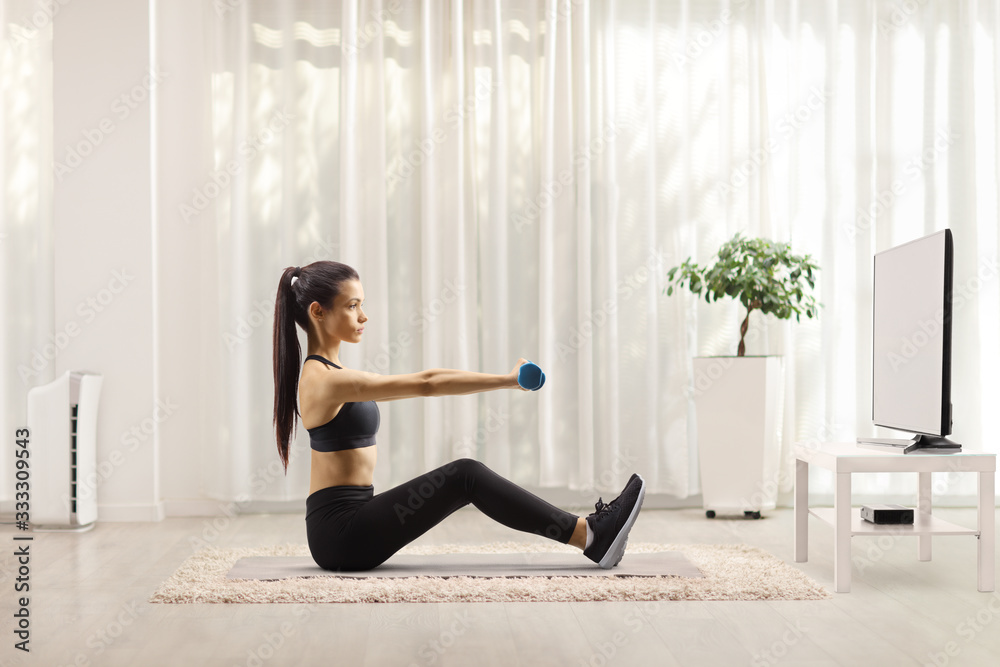 Young woman exercising with dumbbells in front of a tv Young woman exercising with dumbbells in front of a tv