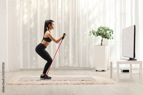 Young woman in sportswear exercising with a resistance band in front of a tv