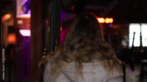 Cheerful and beautiful confident young female in winter jacket opening door and entering bar with a toothy smile during day