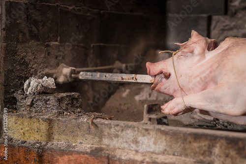 Pig on a metal rod is being prepared to be turned on a traditional balkan grill called rostilj or odojek. Fresh pig waiting on a grill. Detail of rod inserted into mouth. photo