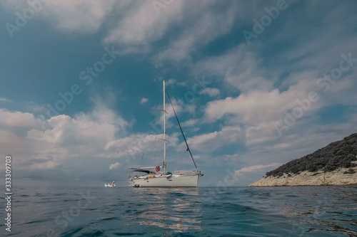 Low profile of a modern sailboat or yacht moored in a beautiful lagoon in adriatic. White sailboat with sails stowed floating in the summer sea