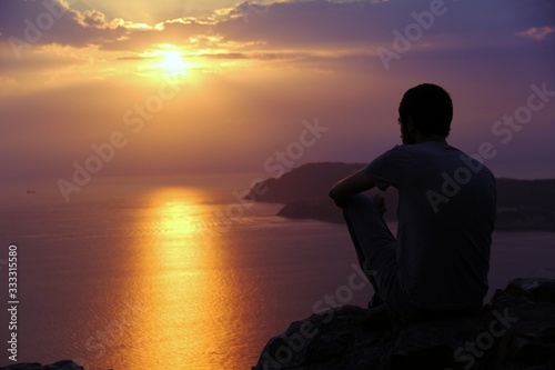 Silhouette of man watch colorful sunset or sunrise in a sea landscape with mountains in the background.