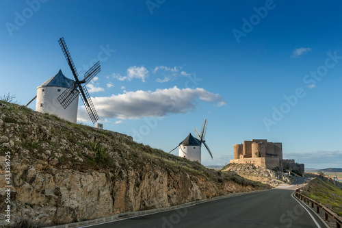 Group of ancient windmills in front of the medieval castle of Consuegra (Spain), on the route of the Don Quixote and Cervantes mills, at sunset.