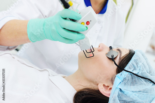 doctor cosmetologist dermatologist conducts a laser skin rejuvenation procedure for a patient-a young pretty woman with a modern fractional laser. Laser cosmetology, removal of scars, scars, photo