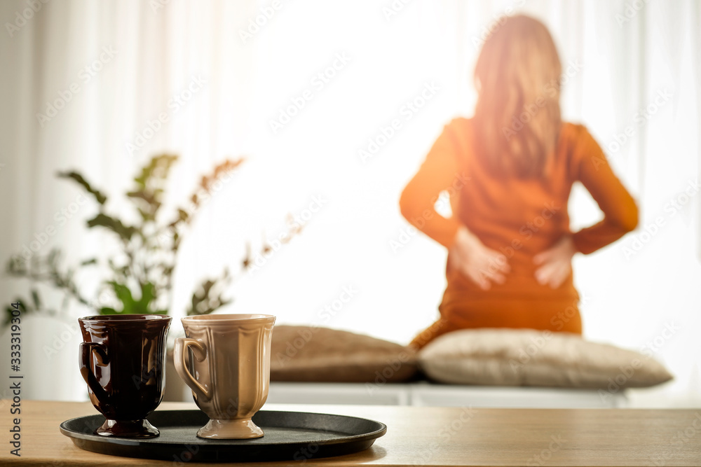 A woman at a sunny window on a wonderful morning behind a wooden table with warm tea A woman at a sunny window on a wonderful morning behind a wooden table with warm tea