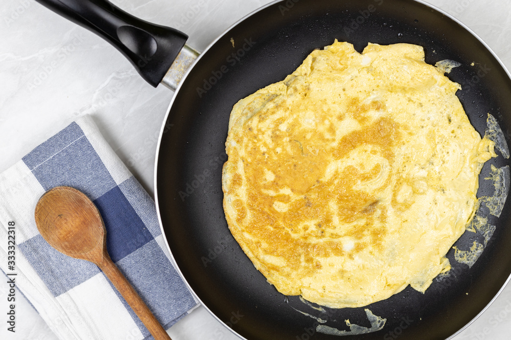Flatlay above fried omelet in the frying pan with dishcloth on the table