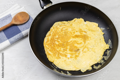 Flatlay above fried omelet in the frying pan with dishcloth on the table