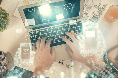 Double exposure of man's hands typing over computer keyboard and flying envelop hologram drawing. Top view. e-mail concept.