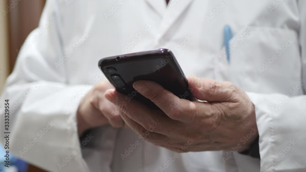 A Man's Hands With Smart Watch Using A Smartphone, Close Up. Elderly Doctor In A White Uniform Holding Mobile Phone, Writes Text.. A Man's Hands With Smart Watch Using A Smartphone, Close Up. Elderly Doctor In A White Uniform Holding Mobile Phone, Writes Text..