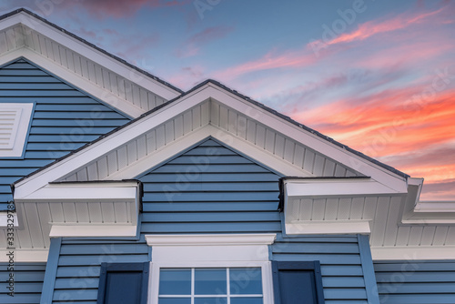 Triangle shape decorative gable with colonial white soffit and fascia on a blue horizontal vinyl siding modern American estate home with colorful dramatic stunning orange sunset sky