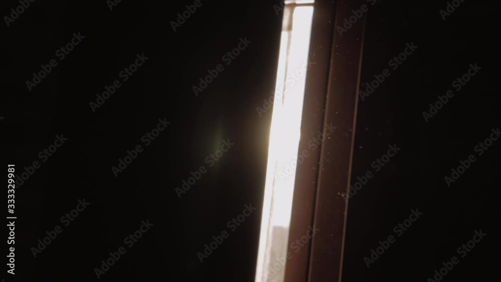 Slow motion shot of flying dust particles with following sunshine coming through the crack of window shutter