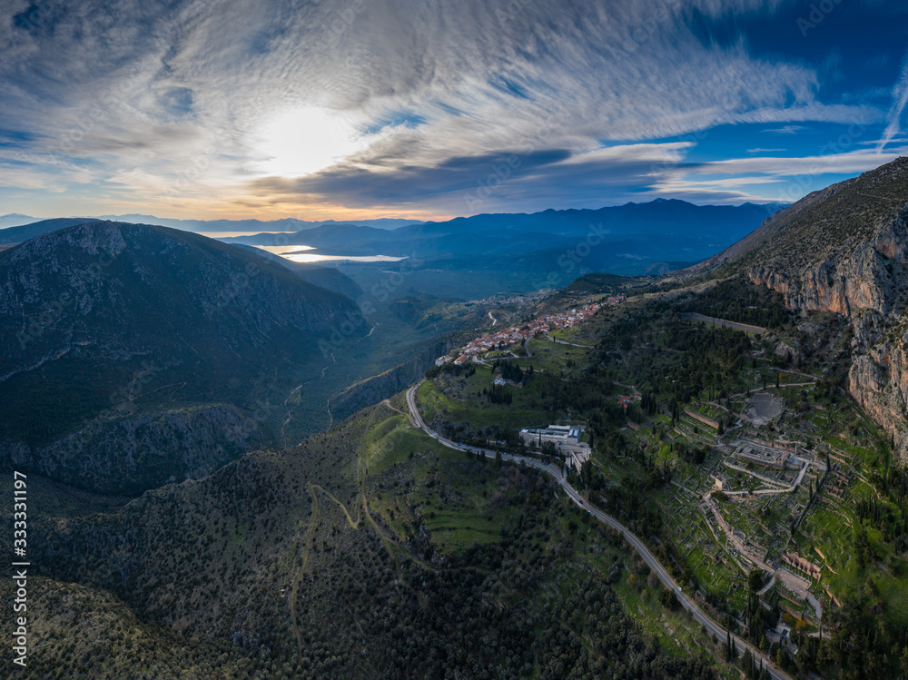 Aerial view of Delphi, Greece, the Gulf of Corinth, orange color of clouds, mountainside with layered hills beyond with rooftops in foreground