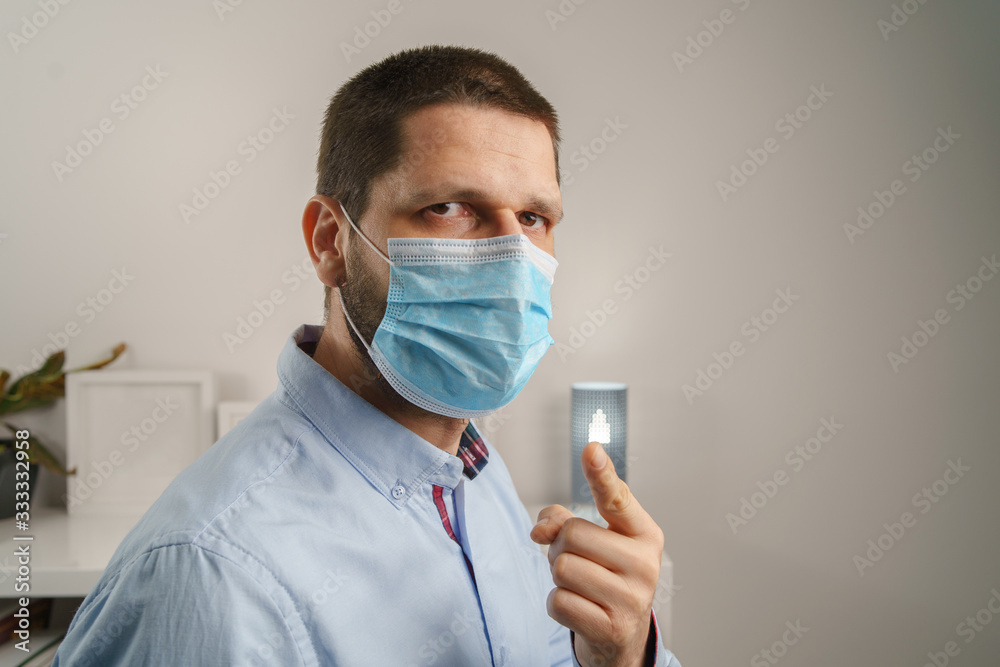 Front view close up portrait of adult caucasian man wearing protective medical mask on his face to protect from virus bacteria or pollution to prevent disease spread looking to the camera point finger