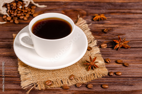 Cup of black aromatic coffee in a white cup with anise stars and cinnamon sticks on a wooden background.
