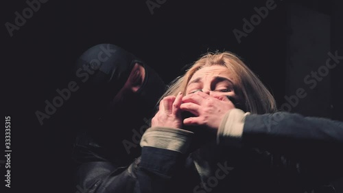 A masked man closes his mouth to a woman. Fear of woman victim of domestic violence and abuse. Violence, crime and kidnapping concept photo