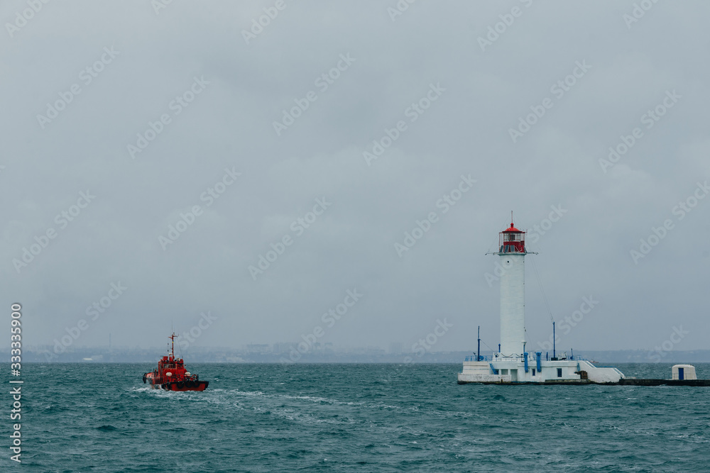 Naklejka premium a small red tugboat swims past the lighthouse in the port