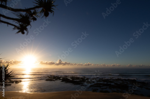 Fototapeta Naklejka Na Ścianę i Meble -  Sun rise at the beach of village of Yeppoon, Queensland, Australia. At the shore of the pacific ocean near Sunshine Coast. Sun rising in between the clouds and reflecting in the water of the sea.  