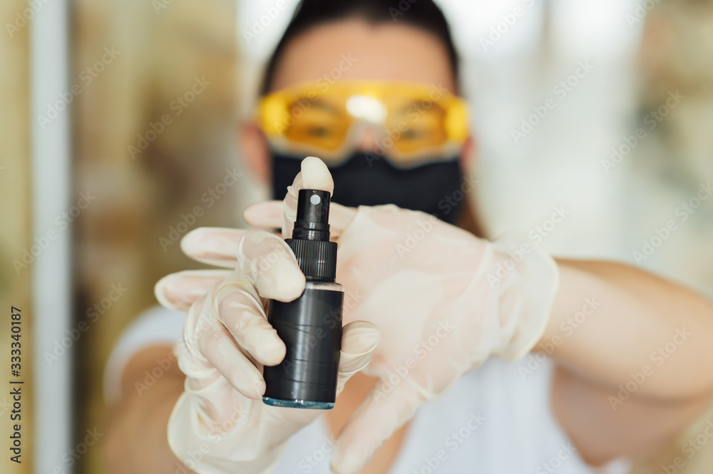 A girl in a protective mask, glasses and gloves spray an antiseptic to prevent infection.