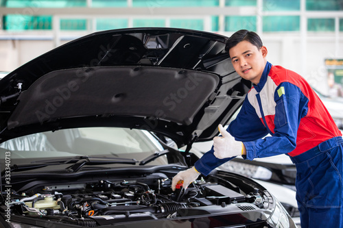 Professional mechanic in uniform is Check the quality of new car before delivering to customers. while working in car repair center.