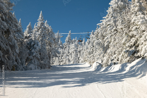 skiers on slope and ski lift with snow covered trees chairlift at background