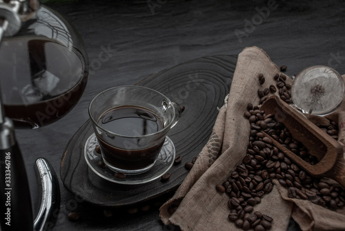 Cup of coffee and coffee beans roating with old wooden scoop and coffee beans around on the wooden and dark stone background. Oblique view from the top with copy space for your text.