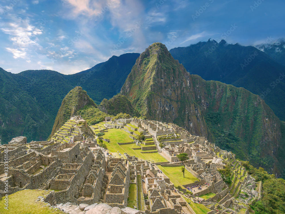 The iconic stone ruins of Machu Picchu and dramatic Huayna Picchu mountain on a sunny day.