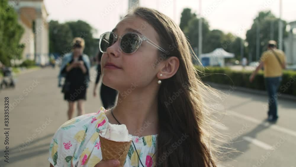Relaxed girl walking in amusement park. Teen girl eating ice cream cone Relaxed girl walking in amusement park. Teen girl eating ice cream cone