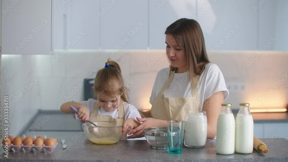 Mother and daughter sowing flour through the sieve into a bowl. Mother teaches daughter to knead a dough. Young mother's assistant. Family business for the production of bread and pies, family bakery. Mother and daughter sowing flour through the sieve into a bowl. Mother teaches daughter to knead a dough. Young mother's assistant. Family business for the production of bread and pies, family bakery.