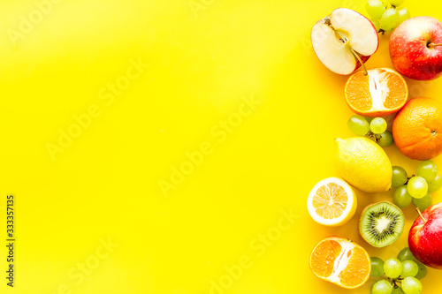 Fresh fruits background with citruses, apple, kiwi and grape on yellow table top-down frame copy space